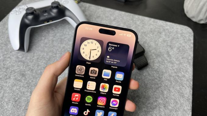 Een hand die een iPhone 14 Pro Max tegen een PS5-controller houdt.